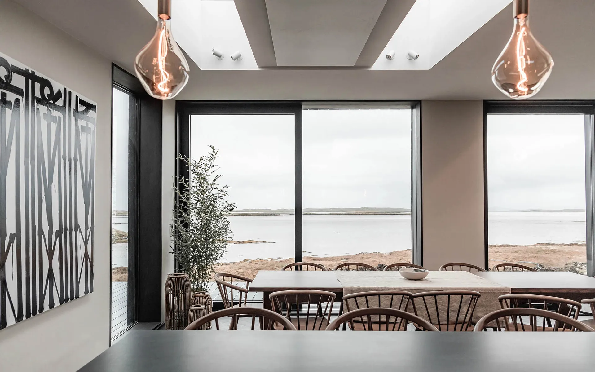 Modern dining room with wooden furniture, glass windows and metal light fixtures.