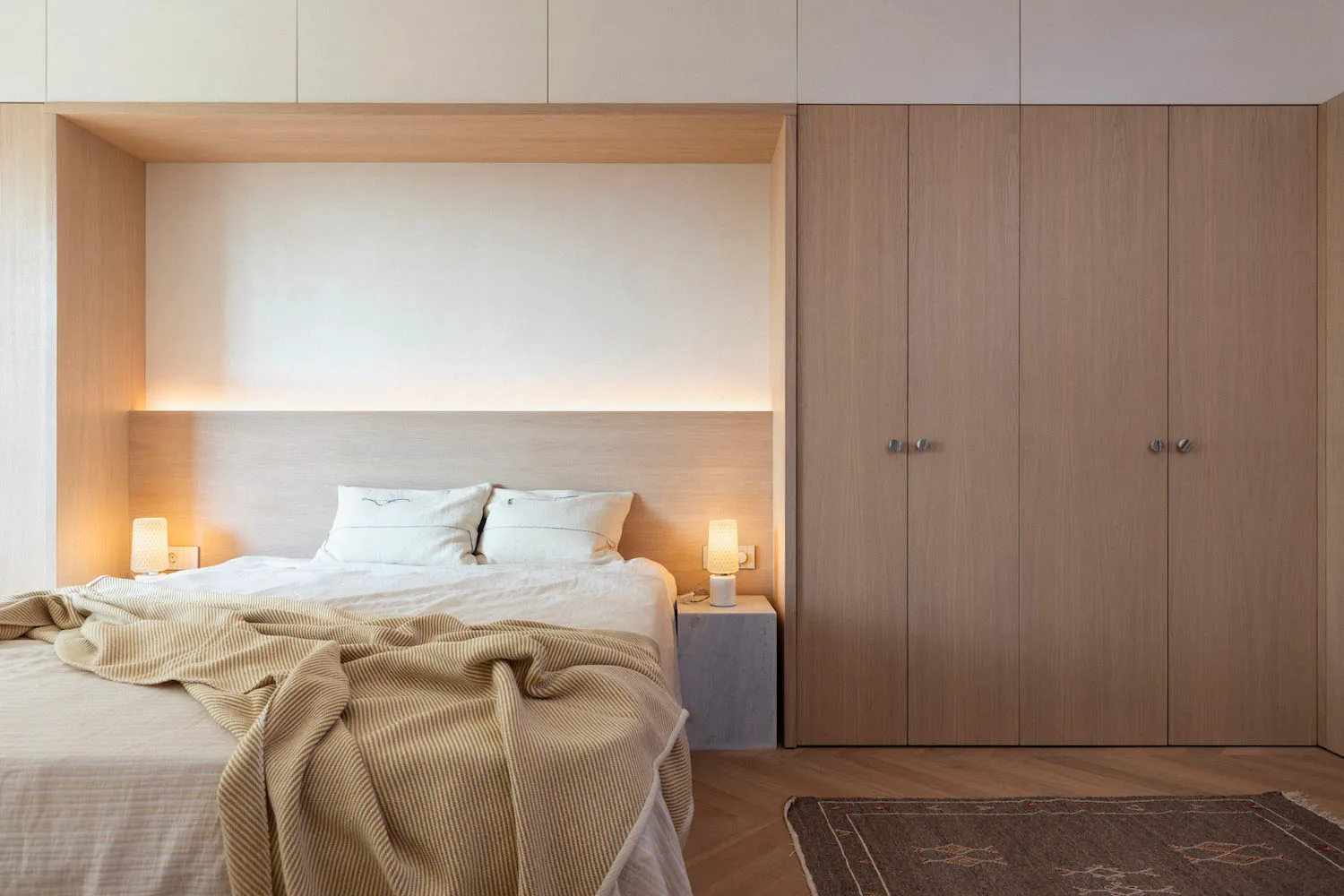 Modern bedroom featuring a bed with wood headboard and concrete floor, illuminated by soft ambient lighting.