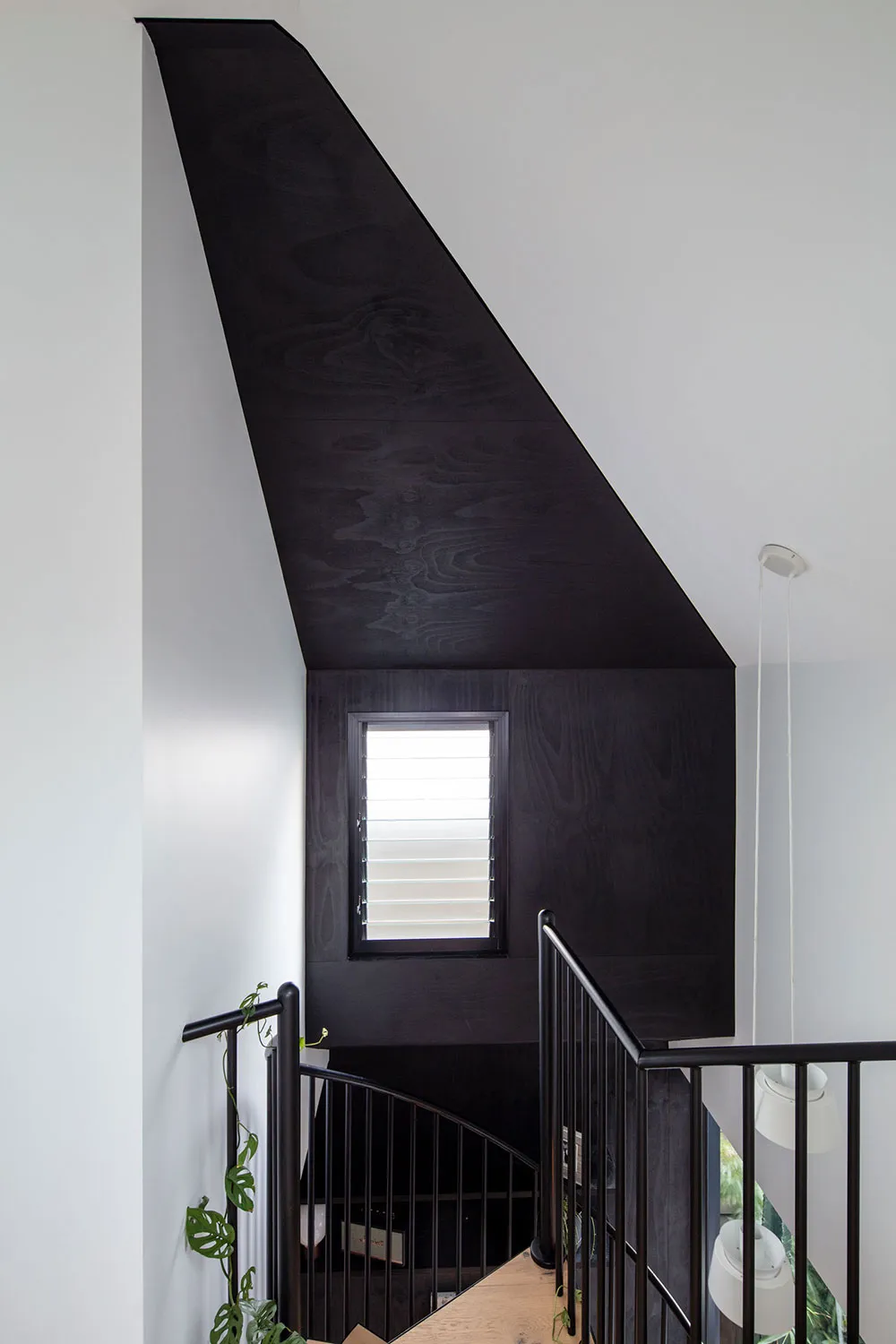 A modern black staircase interior with wooden paneling and a window.