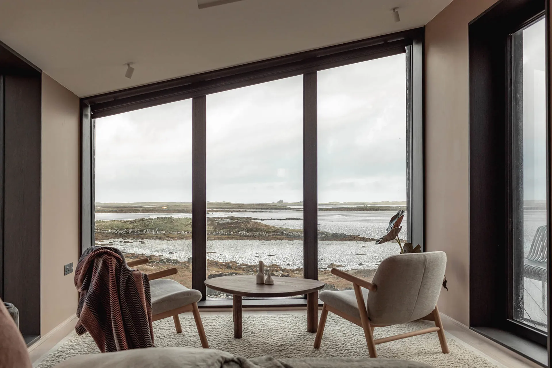 A minimalist living room with a glass wall, wooden furniture, and carpet