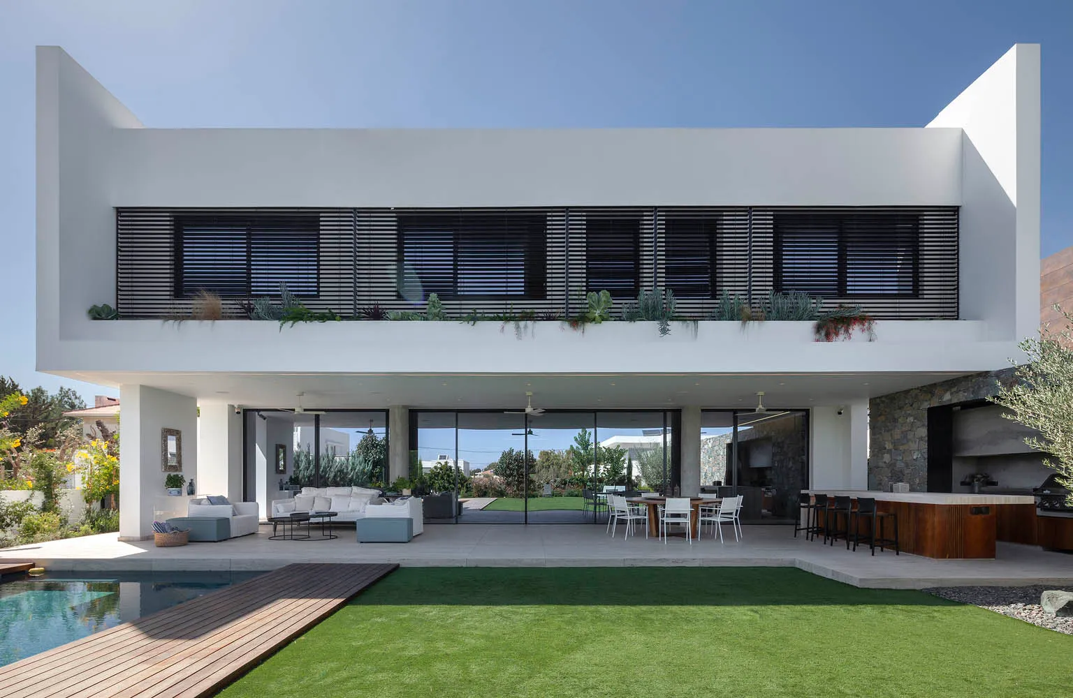 Modern residential space featuring a large patio, swimming pool, and outdoor dining area with a mix of concrete, glass, and w