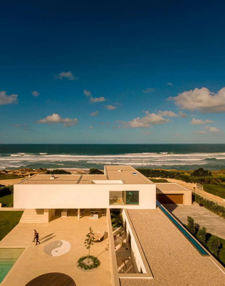 A modern residential house with concrete and glass features overlooking the ocean.