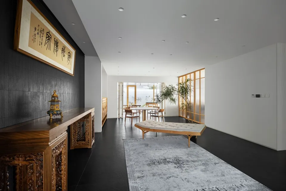 Minimalist living room with white walls, wooden cabinetry, a glass door, and a rug with geometric patterns.