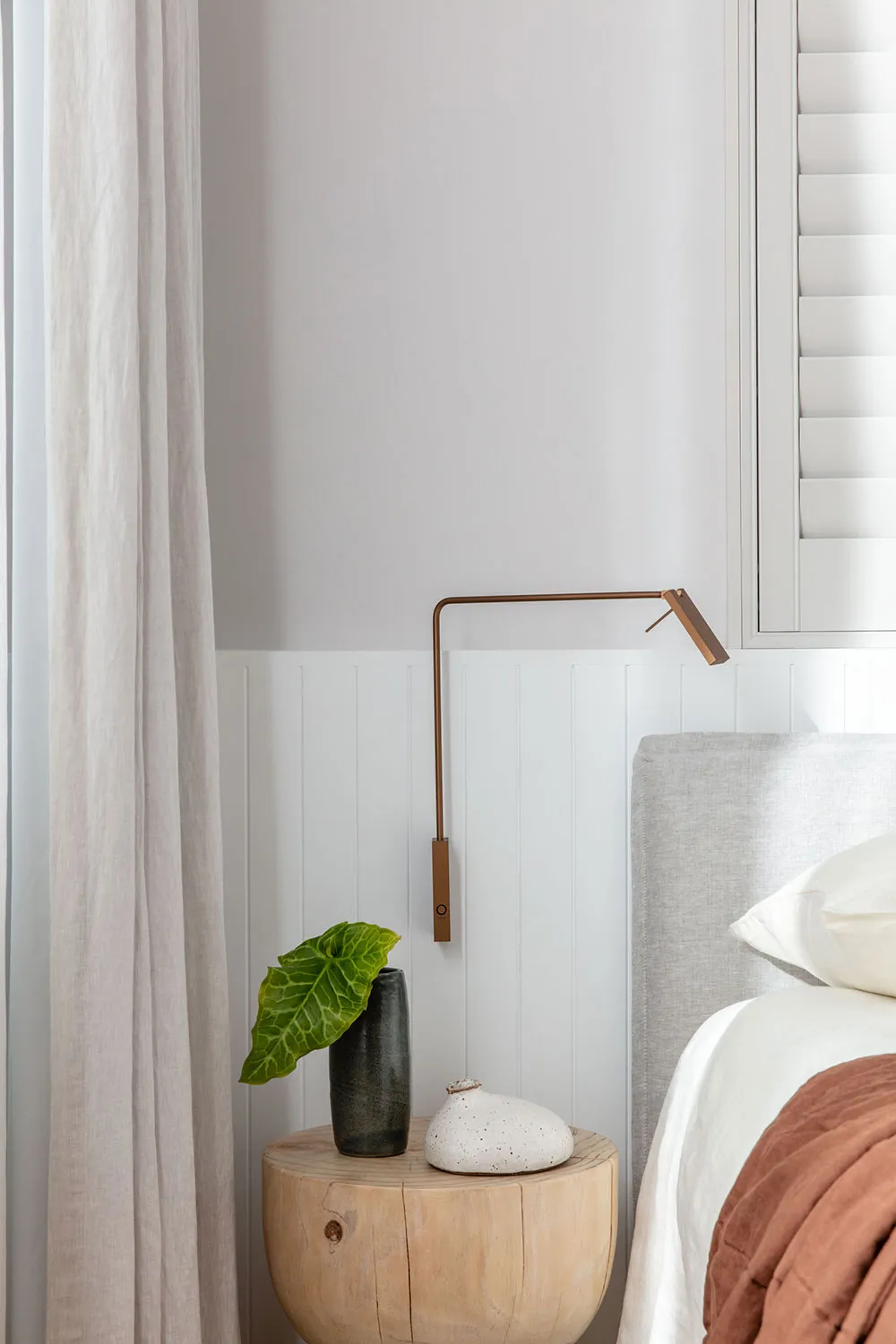 Modern bedroom featuring a wooden stool, a copper pendant lamp, and cotton linens.