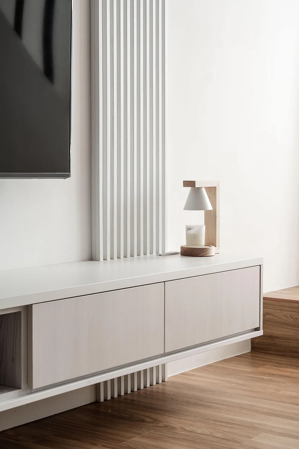 Modern minimalist-style room featuring a sleek white wood cabinet against a white wall and a wooden floor.
