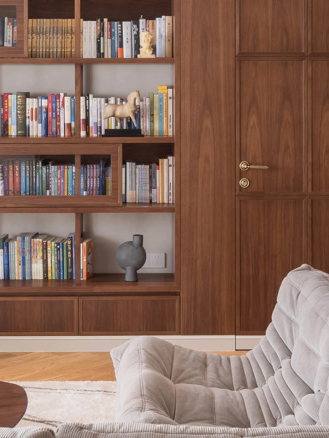 A minimalist living room with a wood bookshelf displaying organized books and decorative objects, accompanied by a cozy fabri