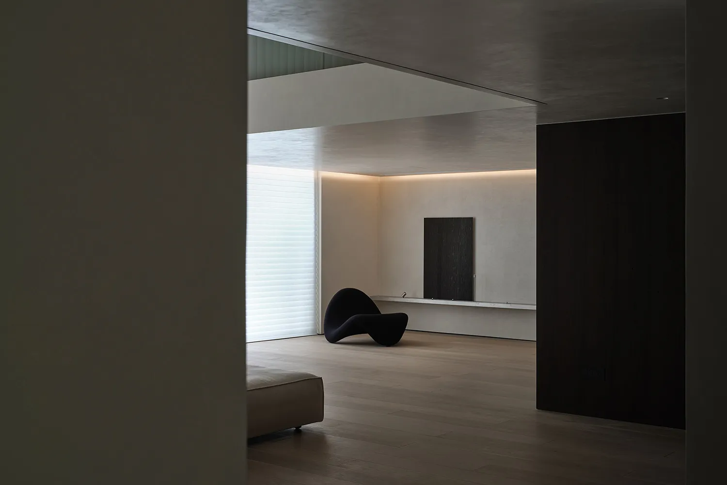 A minimalistic modern living room featuring sleek, black furniture on a wooden floor with soft, ambient lighting.