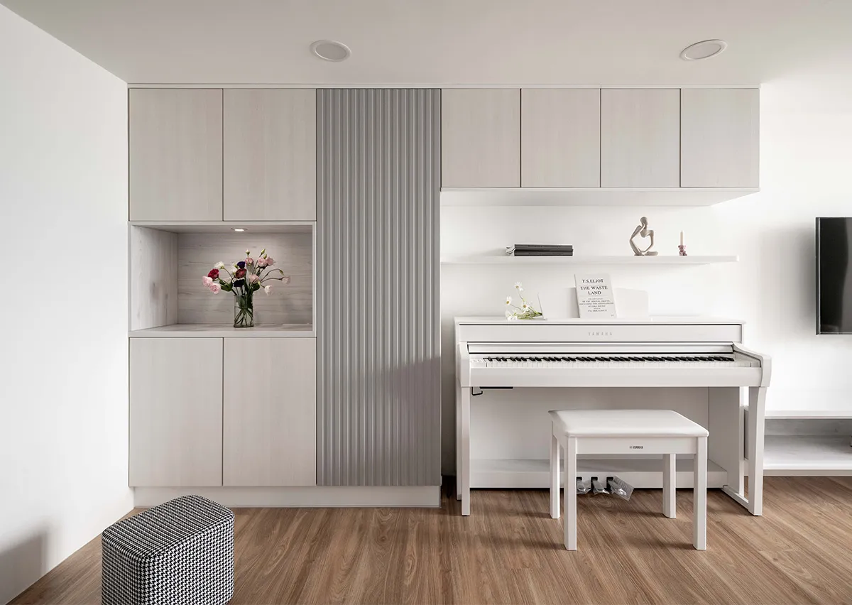 A minimalist room featuring a white Yamaha piano, a wooden stool, and a cabinet with floral arrangements.