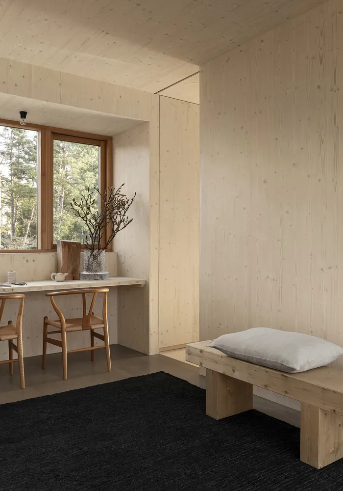 Minimalist bedroom with wooden walls, a wooden bench, and a black rug.