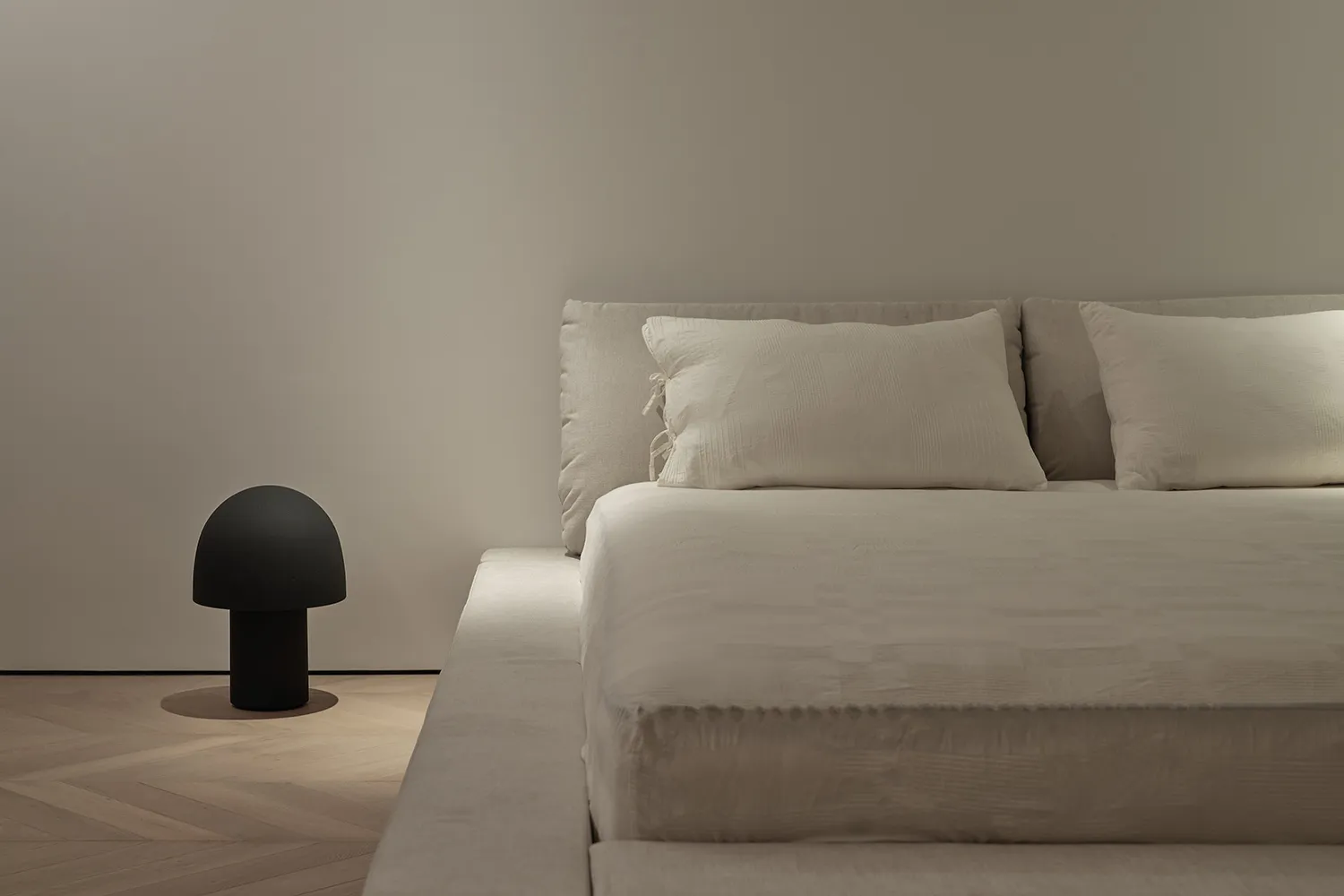 A minimalist white bedroom featuring a fabric bed with a simple, elegant headboard and side table.