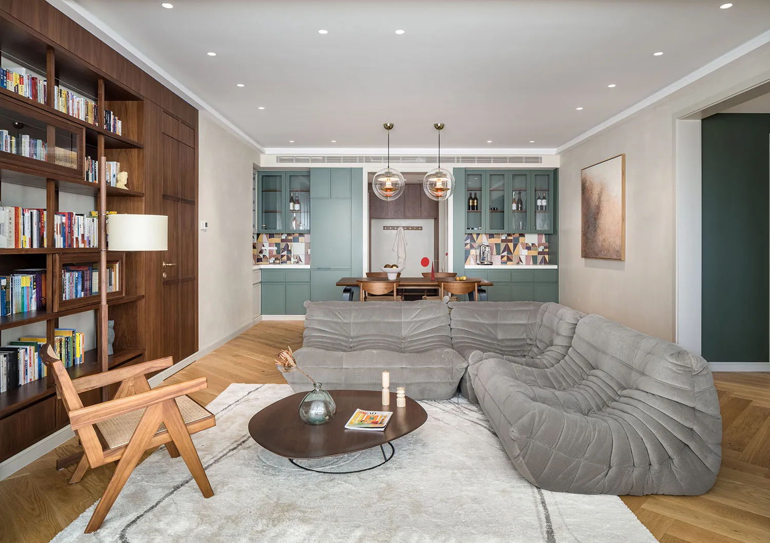 A modern living room featuring a grey sectional sofa, wooden coffee table, and a bookshelf filled with books.