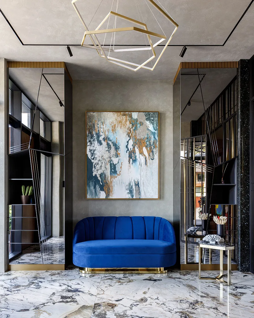 A modern living room with a blue velvet couch, a geometric chandelier, and a large abstract painting on the wall.