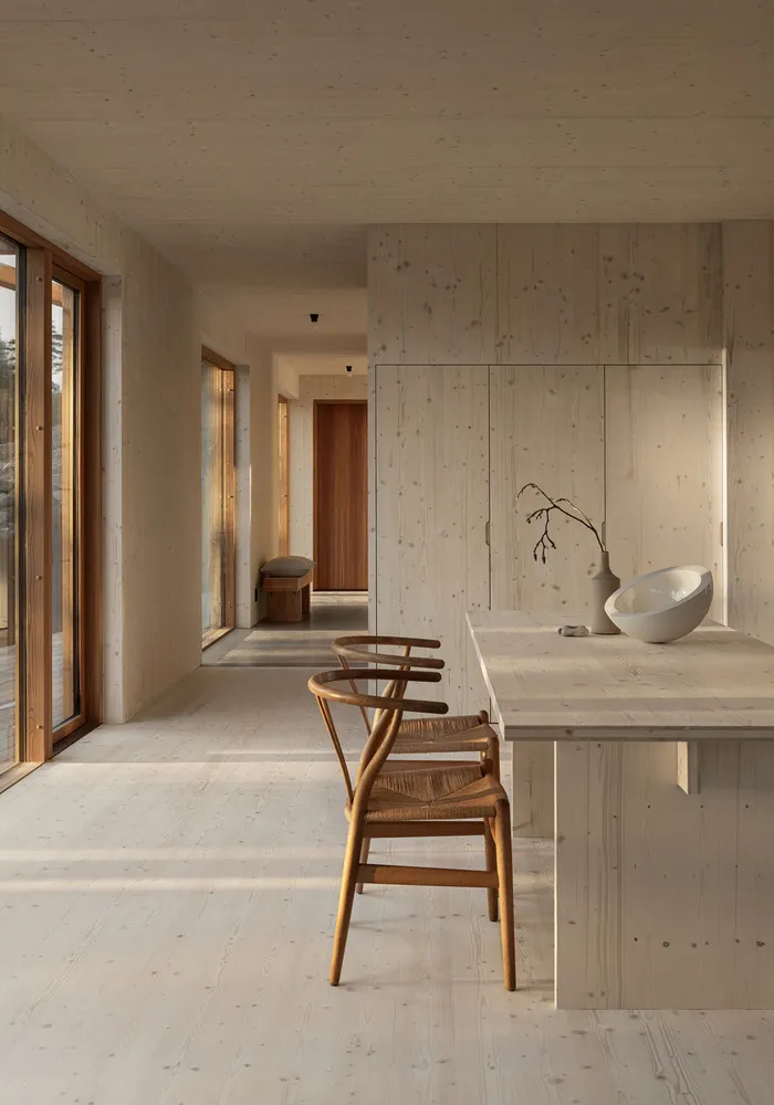 A modern minimalist kitchen featuring wooden finishes and a central island with a white bowl and vase.