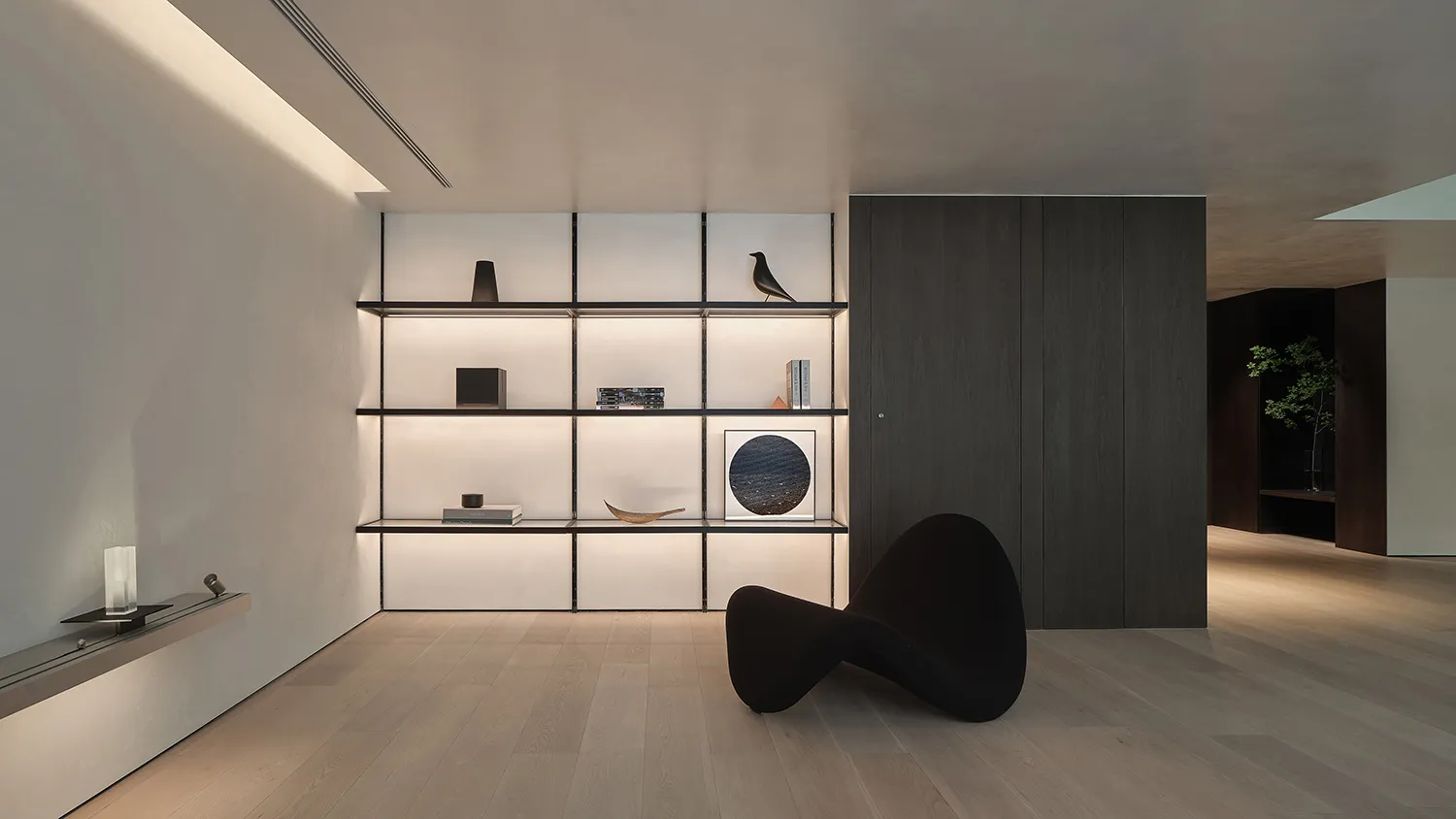 A minimalist living room featuring modern metal shelving with a single black sculptural chair, illuminated by hidden lighting