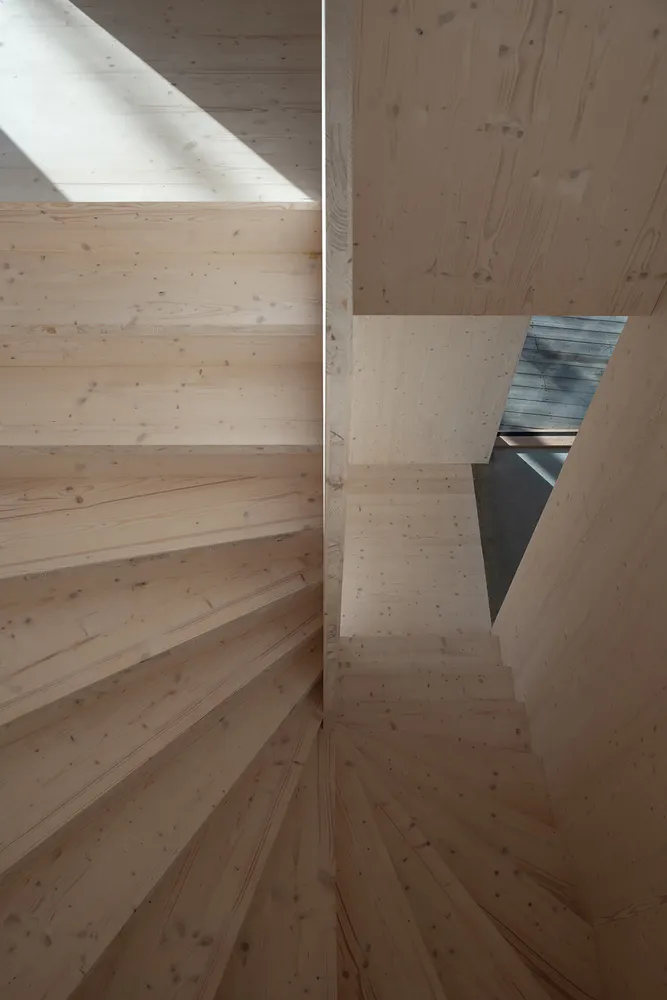 A modern, wooden staircase with a geometric design and natural light coming through a skylight.