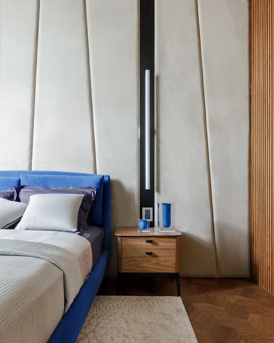 A modern bedroom featuring blue textured wall panels, a wooden nightstand, and a bed with white bedding.