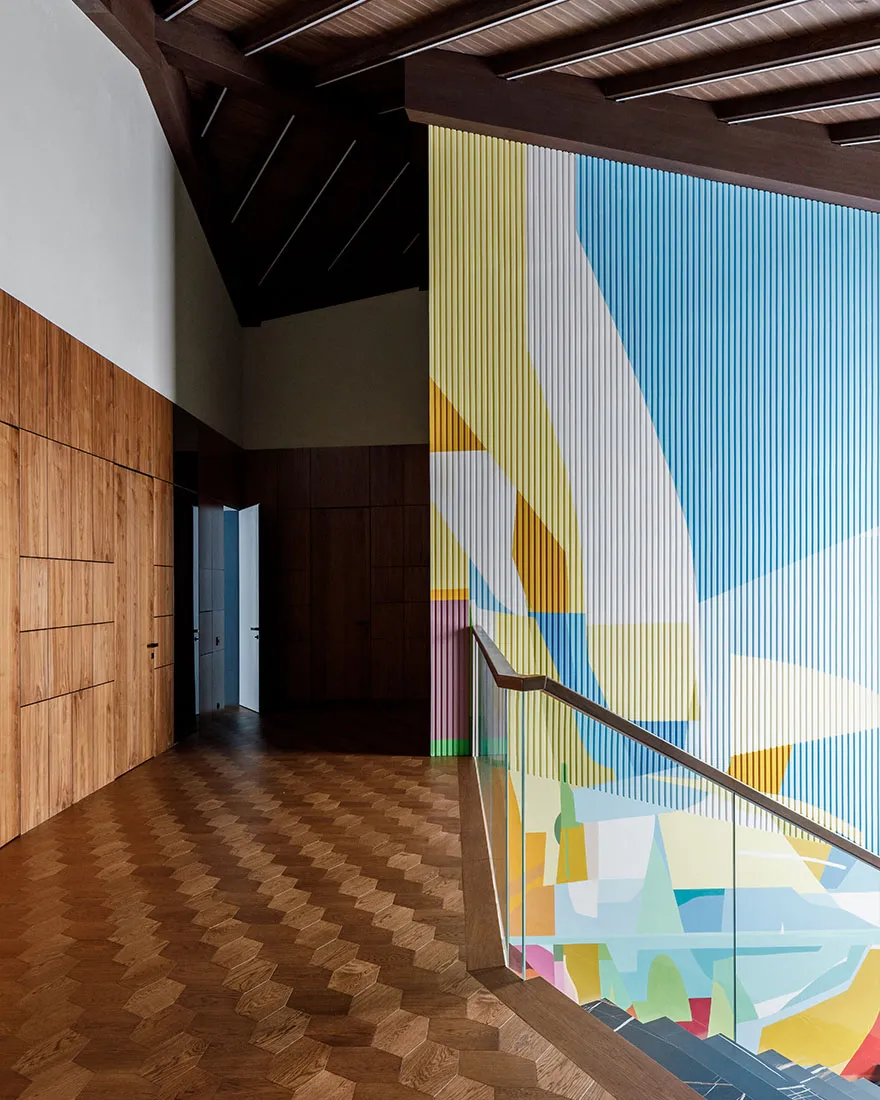 A modern corridor features a colorful abstract print wall and wooden flooring.