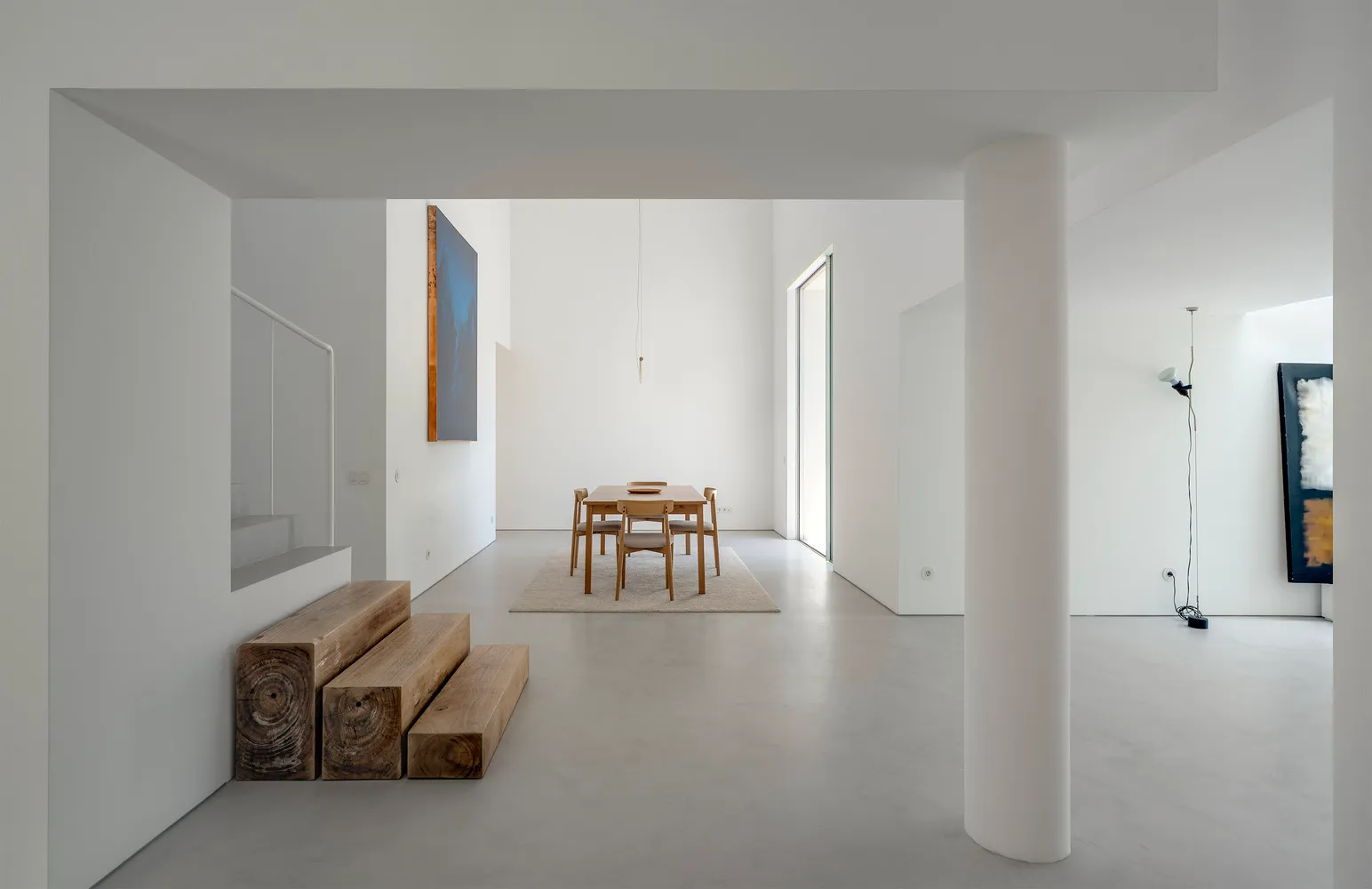 A minimalist living room with concrete walls and floor, featuring a dining table and chairs on a rug.