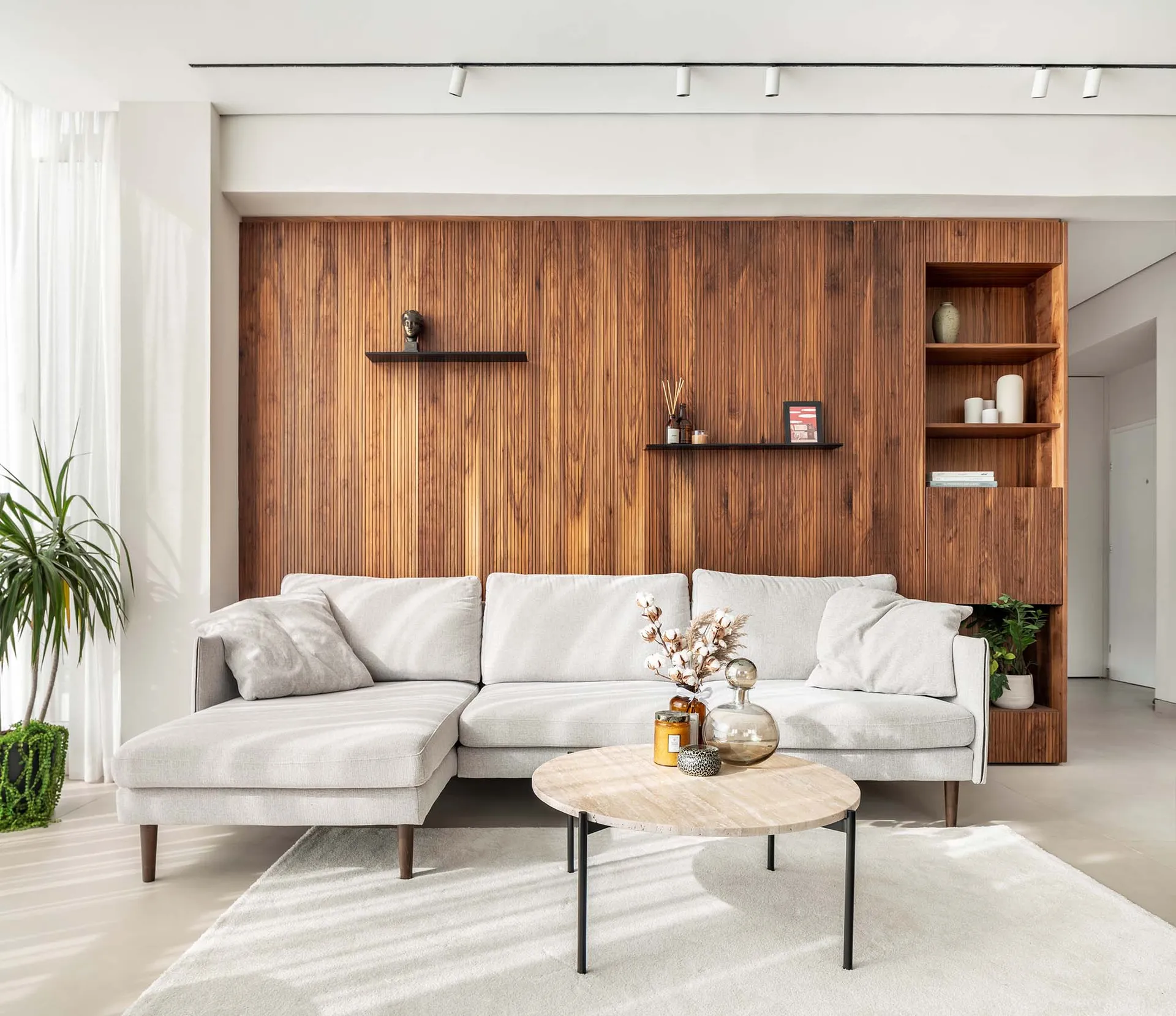 A modern living room featuring a white sofa and a wooden accent wall with floating shelves.