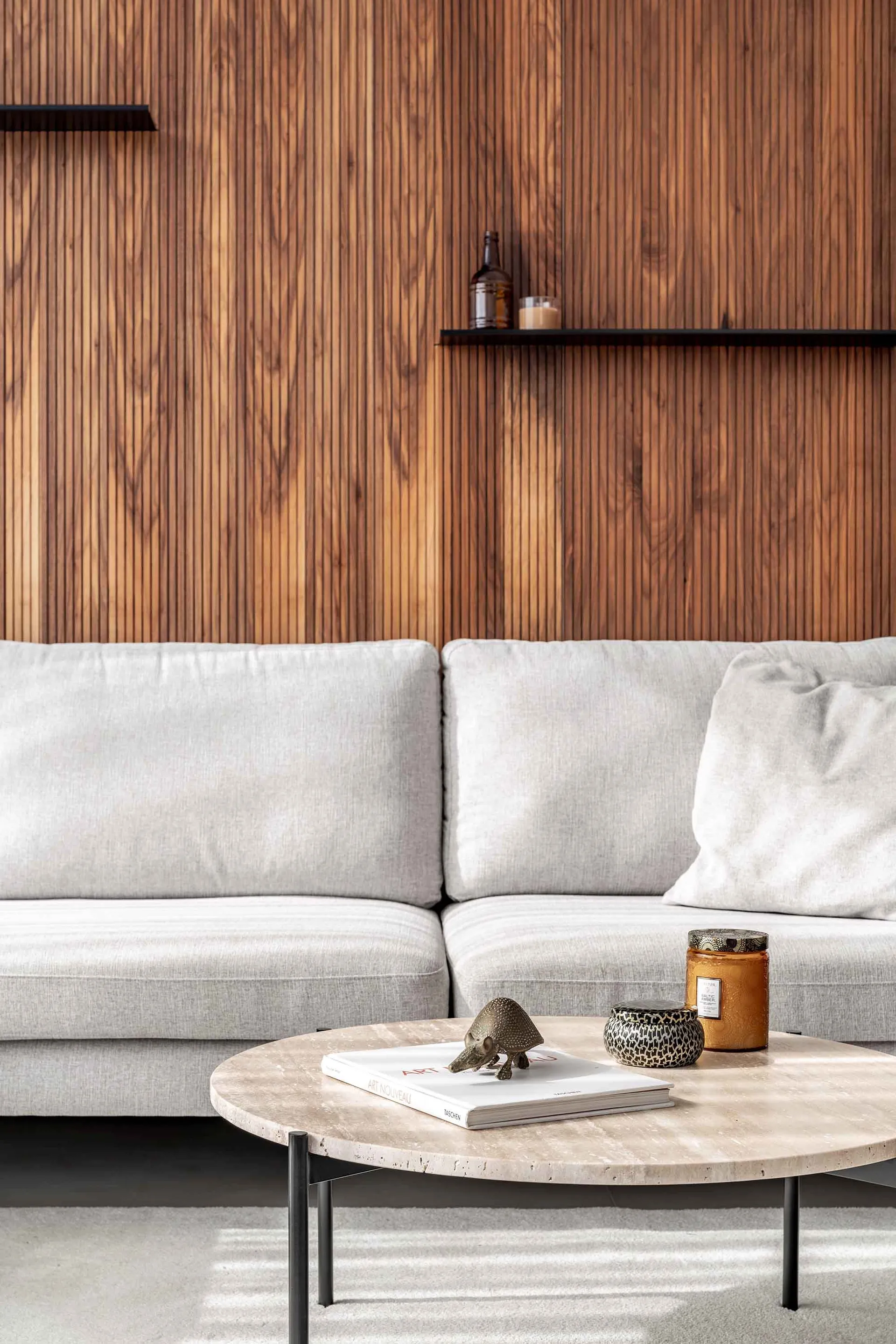 A modern living room with a white couch, wooden paneling, and a coffee table with decorative items.