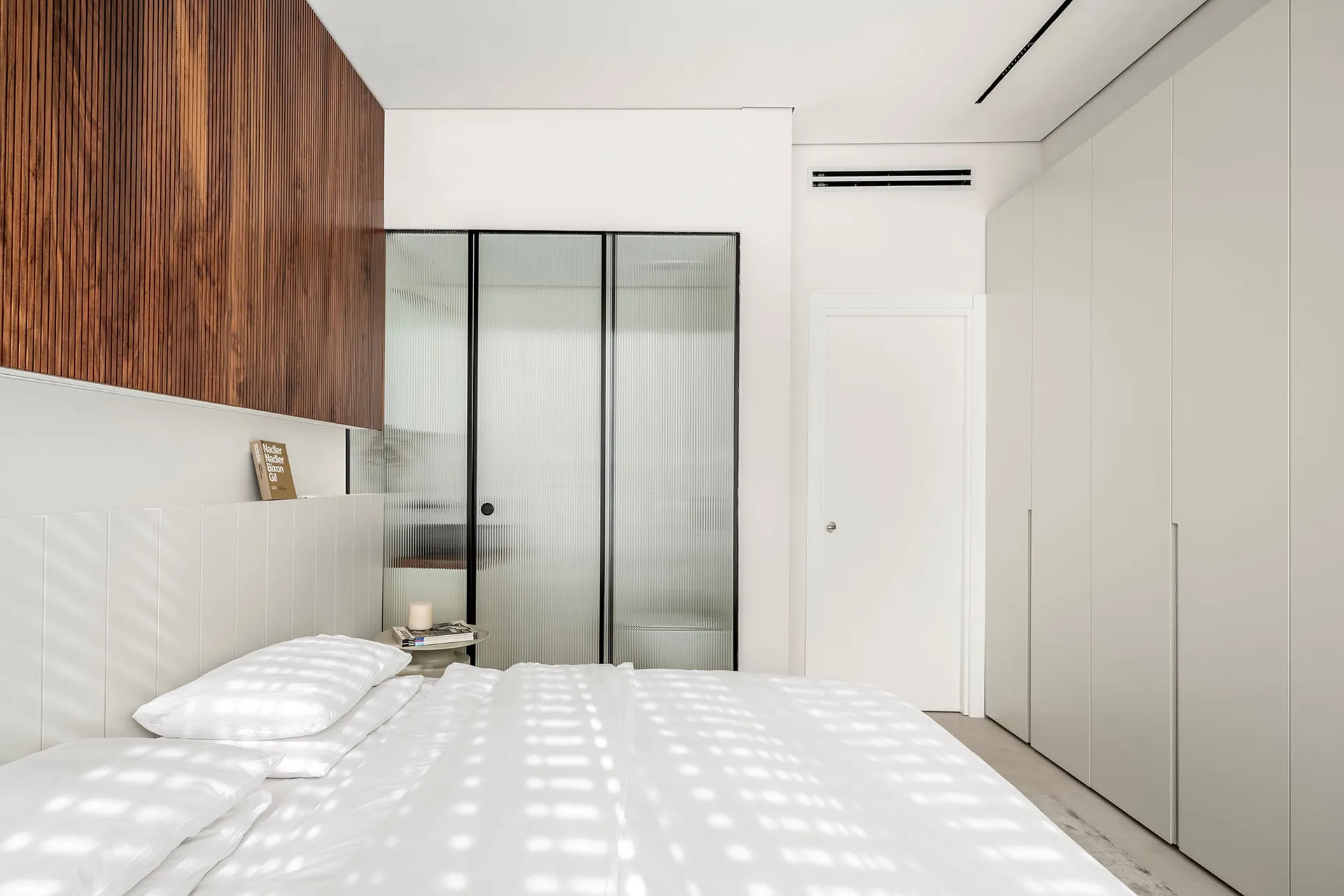 A minimalist bedroom featuring glass walls and a white bed with wooden accents.