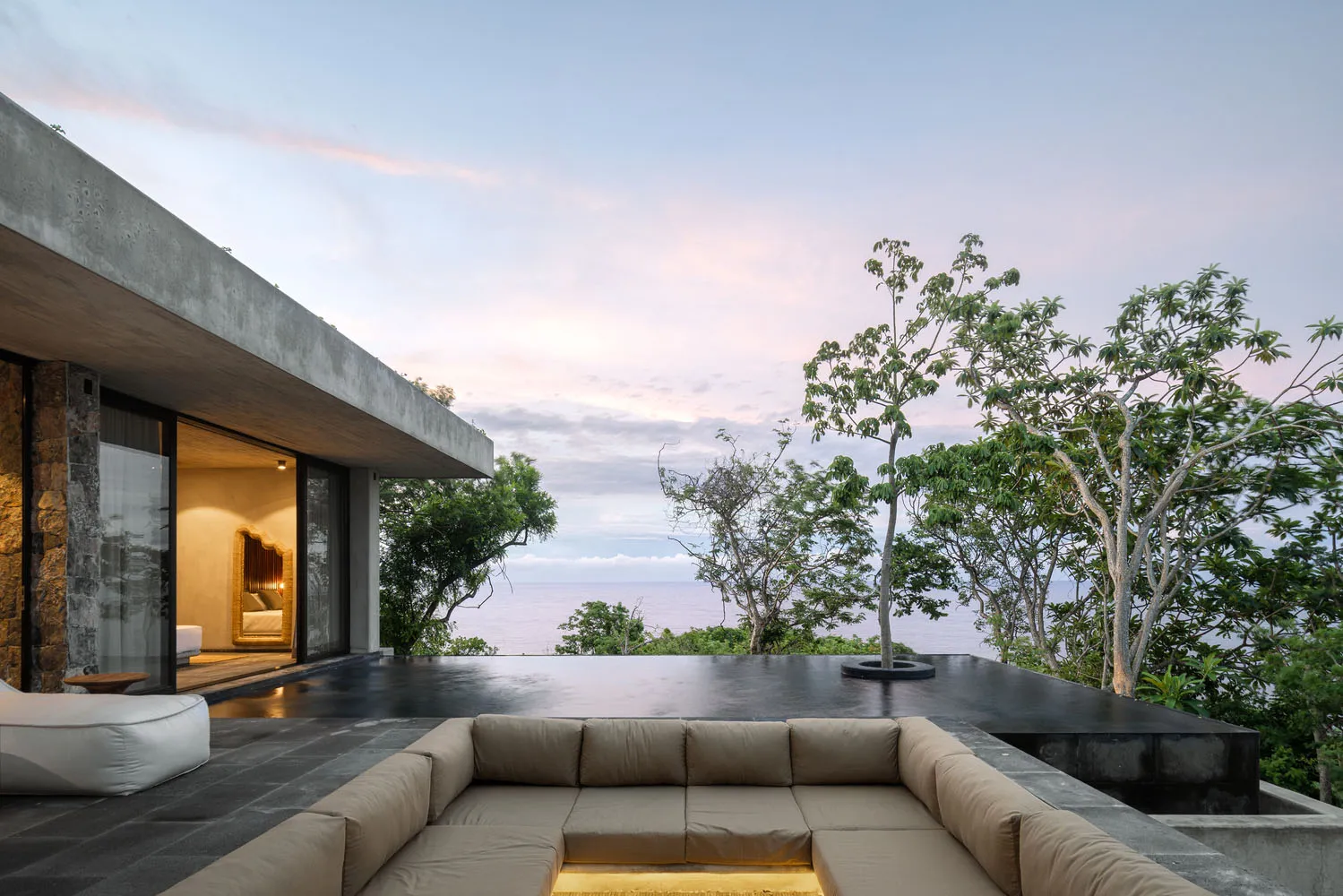 A modern residential exterior featuring a concrete house with large windows and an infinity pool overlooking the ocean.