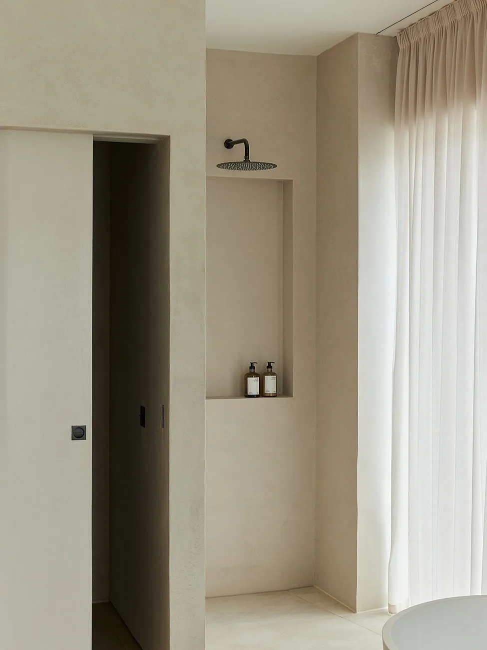 A minimalist bathroom featuring a concrete shower space with a built-in niche, a rain showerhead, and beige tiles on the floo