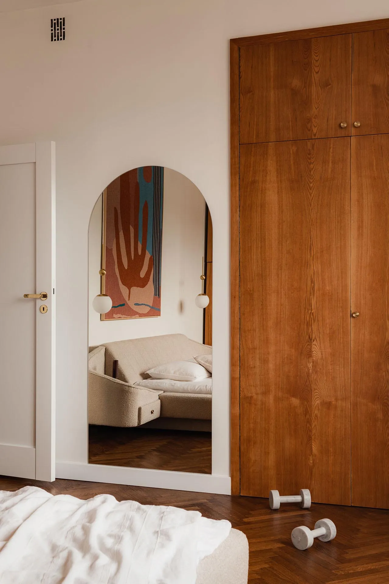 Modern minimalist bedroom with wooden wardrobe, fabric bed, and decorative mirror