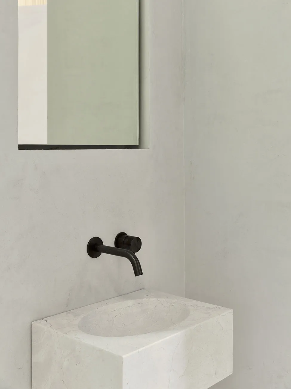 Modern bathroom featuring a minimalist white marble sink with a black faucet and a rectangular mirror on the wall.