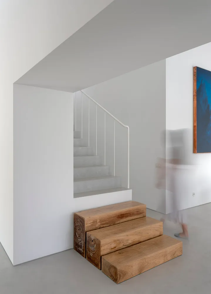 A minimalist staircase with wooden steps and a white concrete wall in a white, empty space.