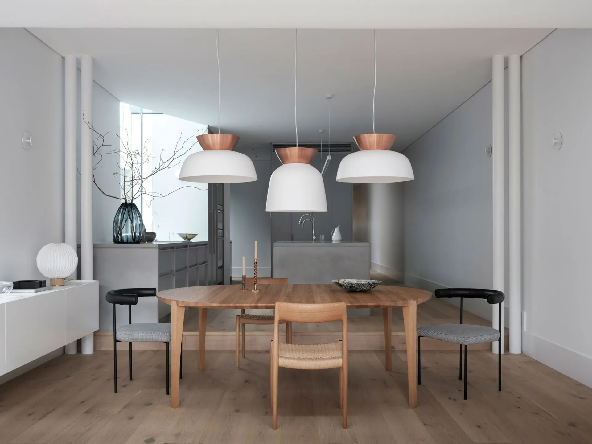 Modern dining room with wooden table, concrete wall, and copper pendant lights.