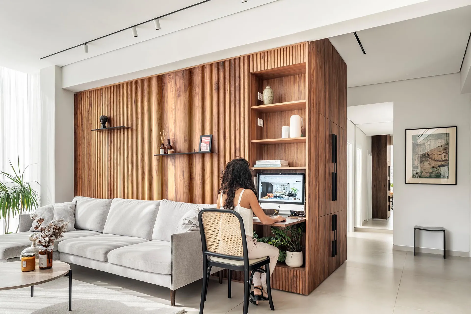 A modern living room with a white sofa and a wooden desk with a computer.