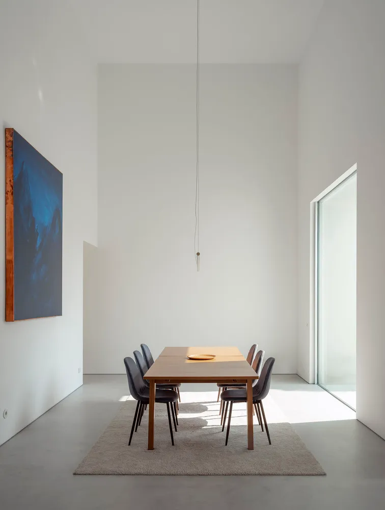 Modern minimalist dining room with a wooden table and chairs, featuring a large abstract painting and natural light streaming