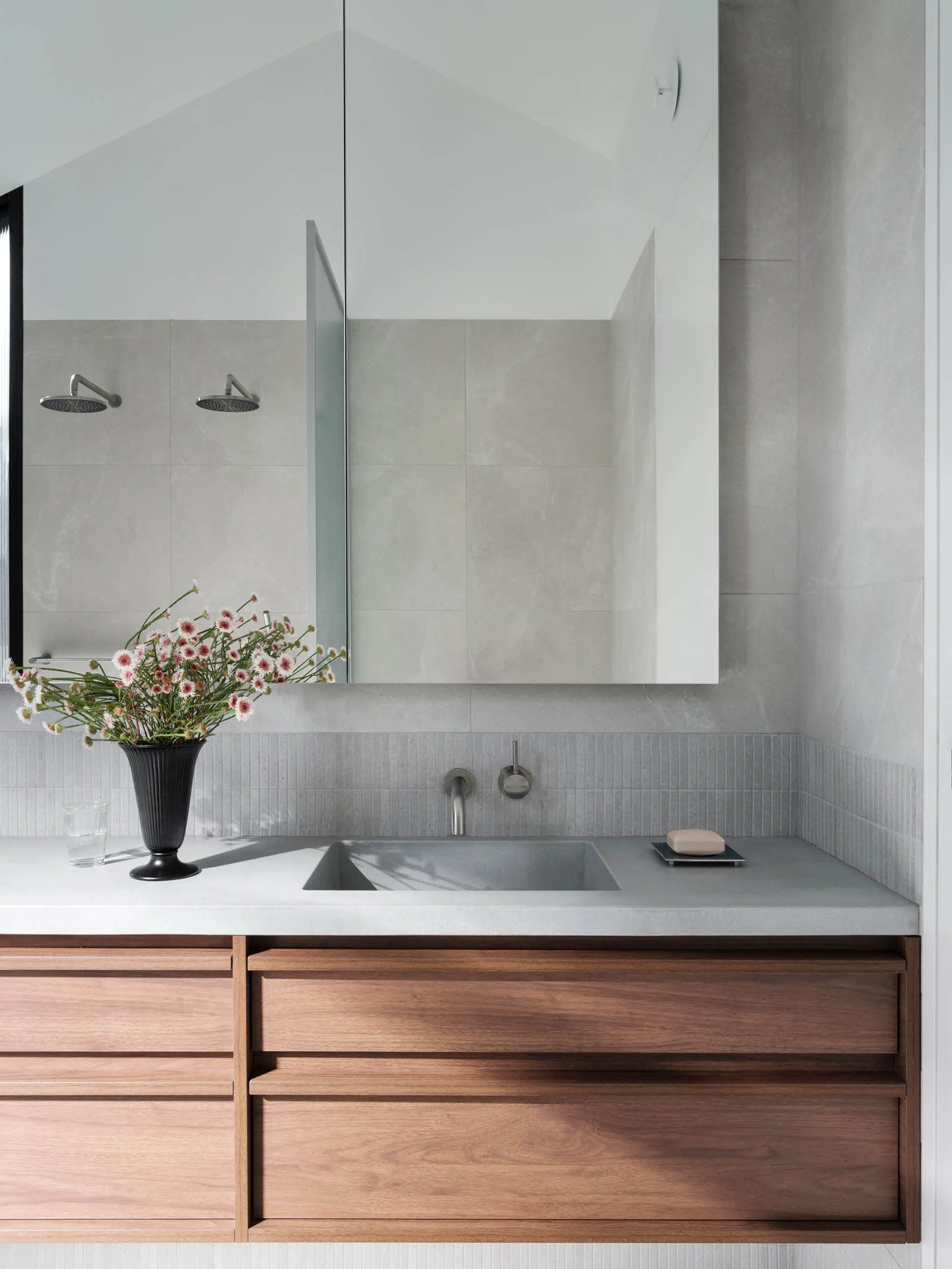 A modern minimalist bathroom with concrete walls, wooden vanity, and a vase of flowers on the sink counter.