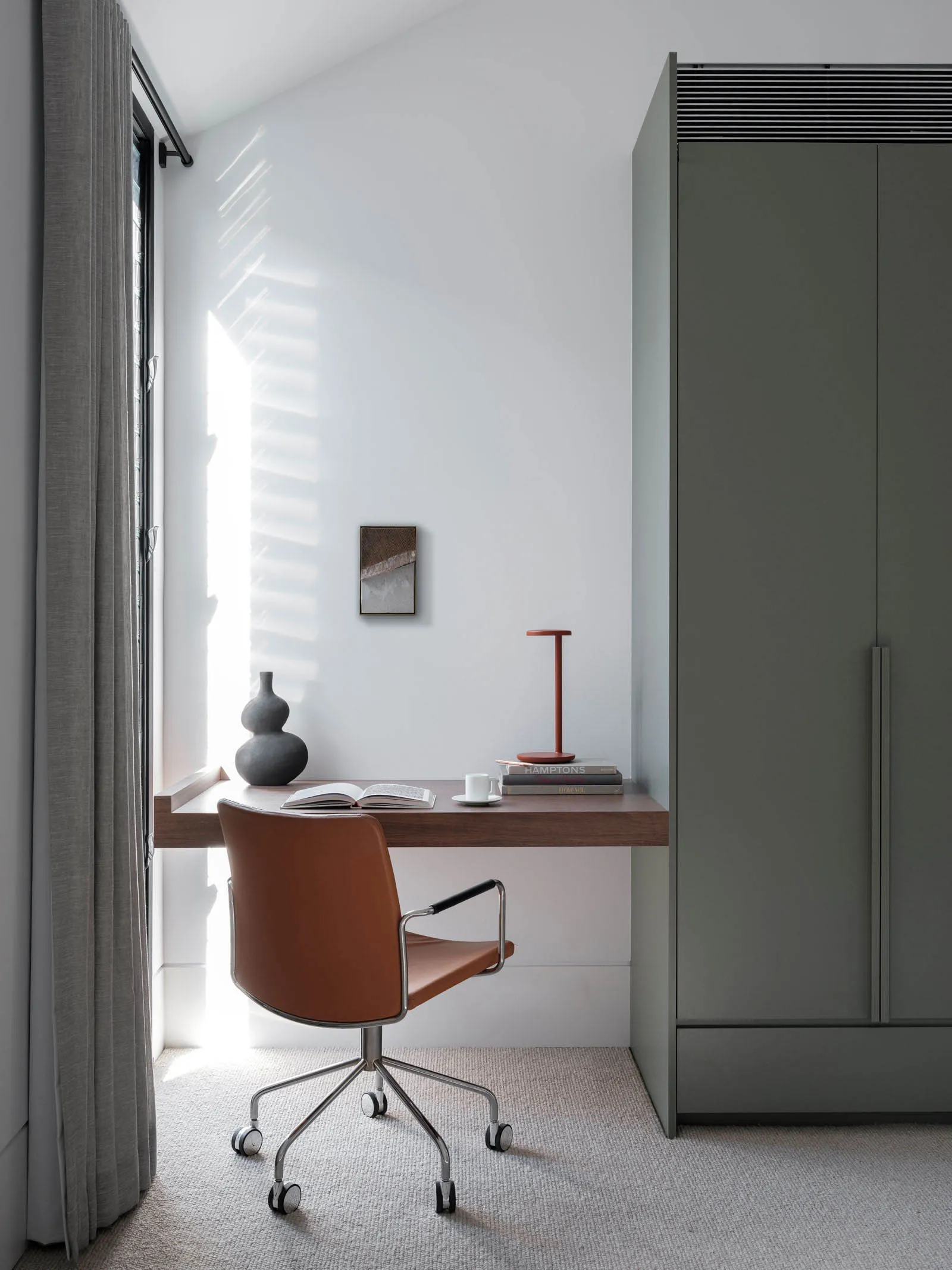 A minimalist home office setup with a wooden desk, brown leather chair, and white walls.