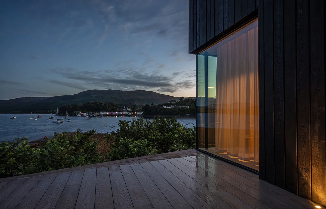 A serene riverside view at dusk with a large glass window draped with orange curtains, reflecting the twilight sky.