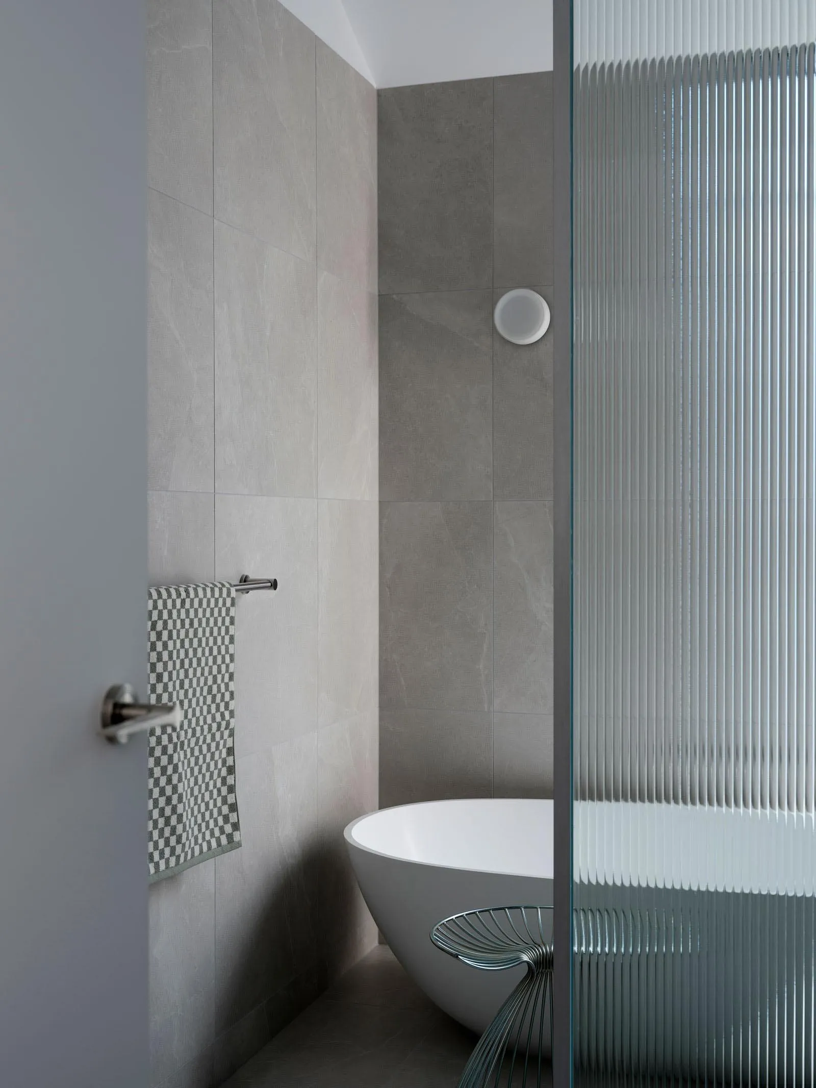 A modern bathroom with grey tiled walls, a freestanding bathtub, and a sleek shower enclosure.