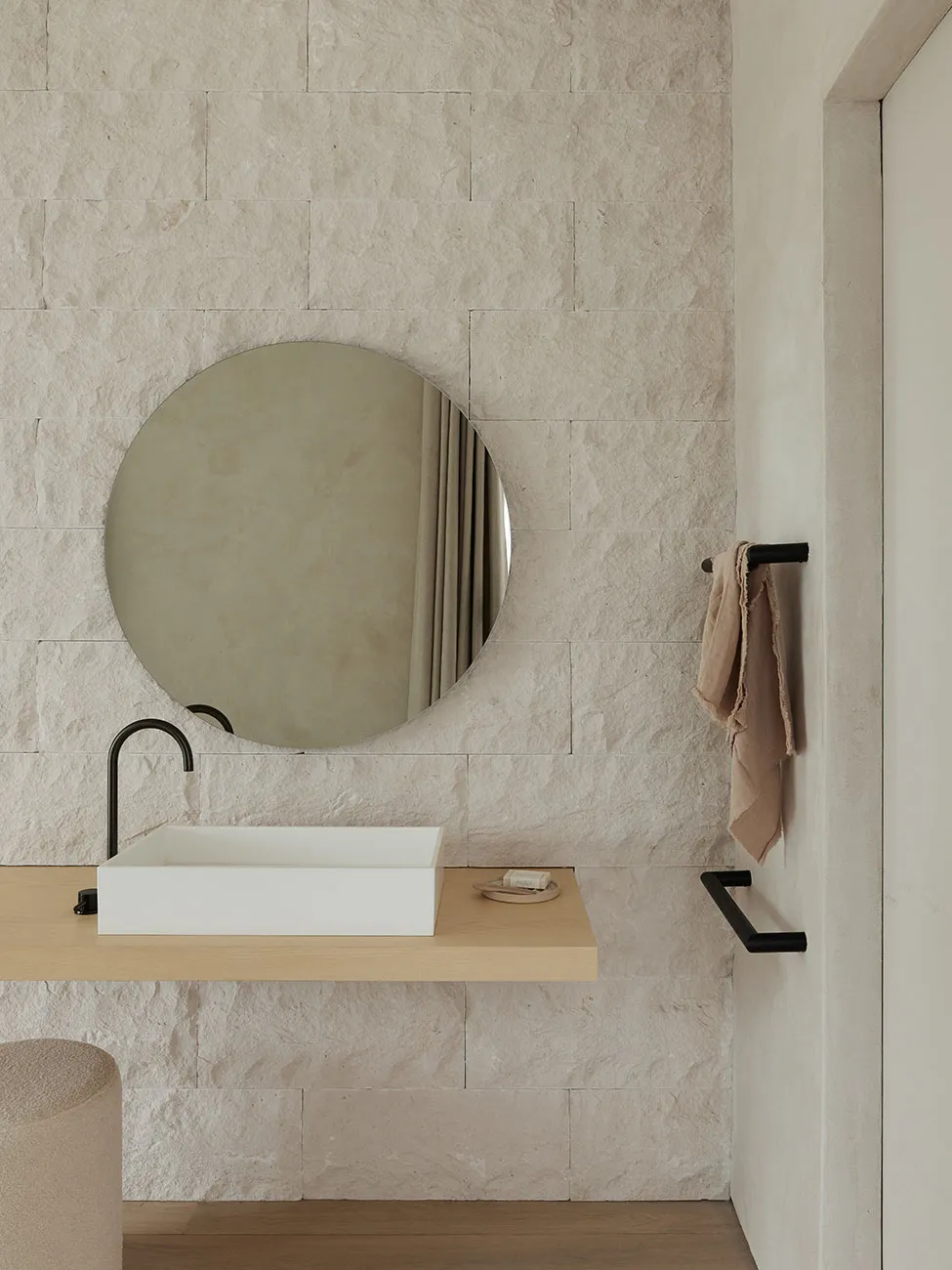 Modern minimalist bathroom with stone walls, a round mirror, a rectangular sink, and a towel bar.