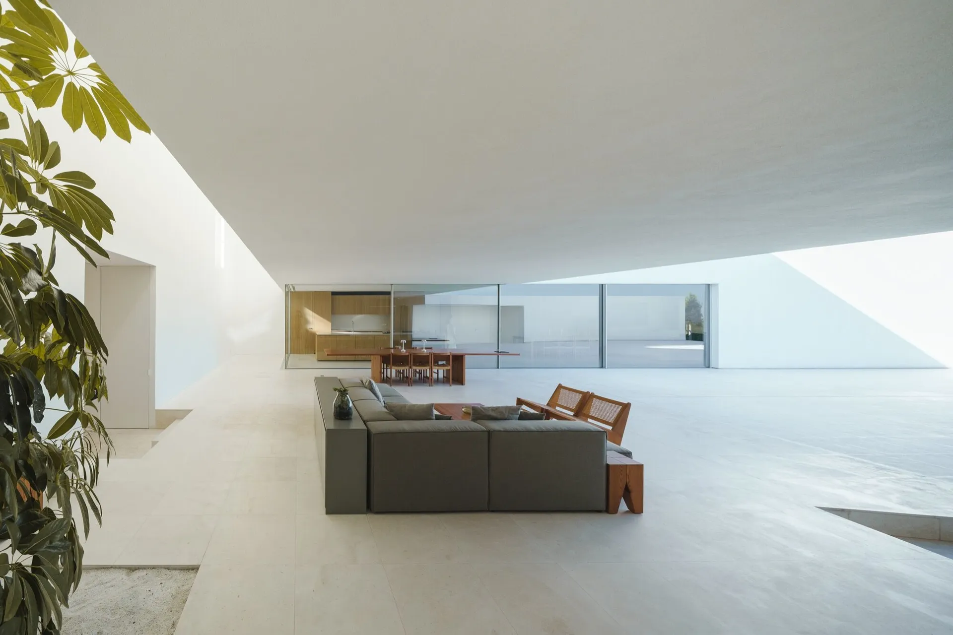 Modern living room with concrete floor and minimalist furniture, glass doors, and large windows.