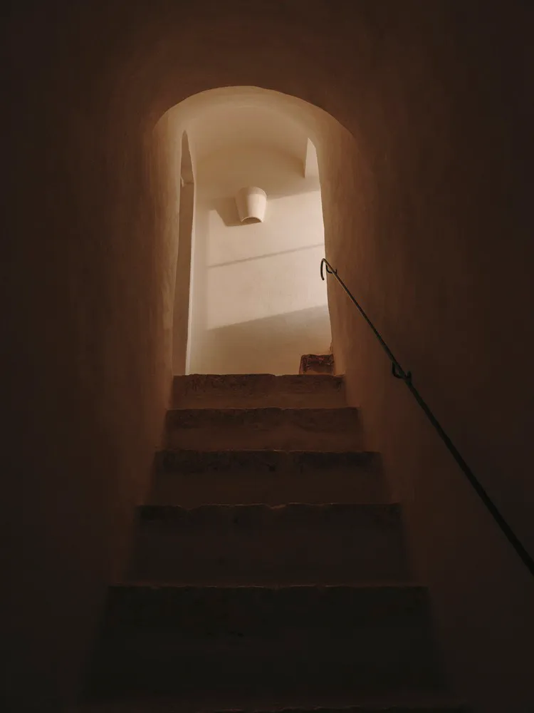 A narrow stone staircase with a metal railing in an indoor building.