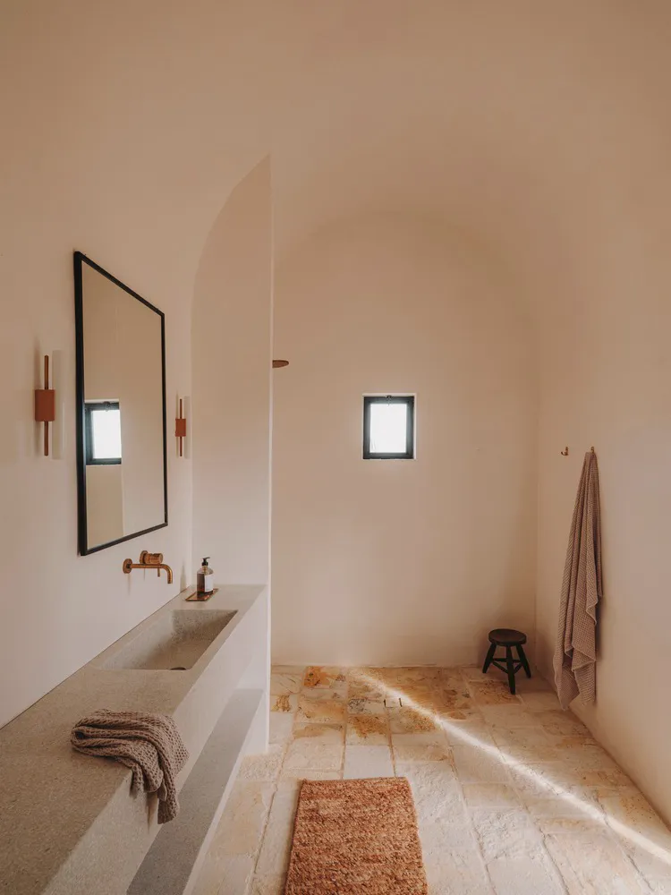 Modern minimalist bathroom featuring a concrete sink and floor, with a large mirror and natural light.