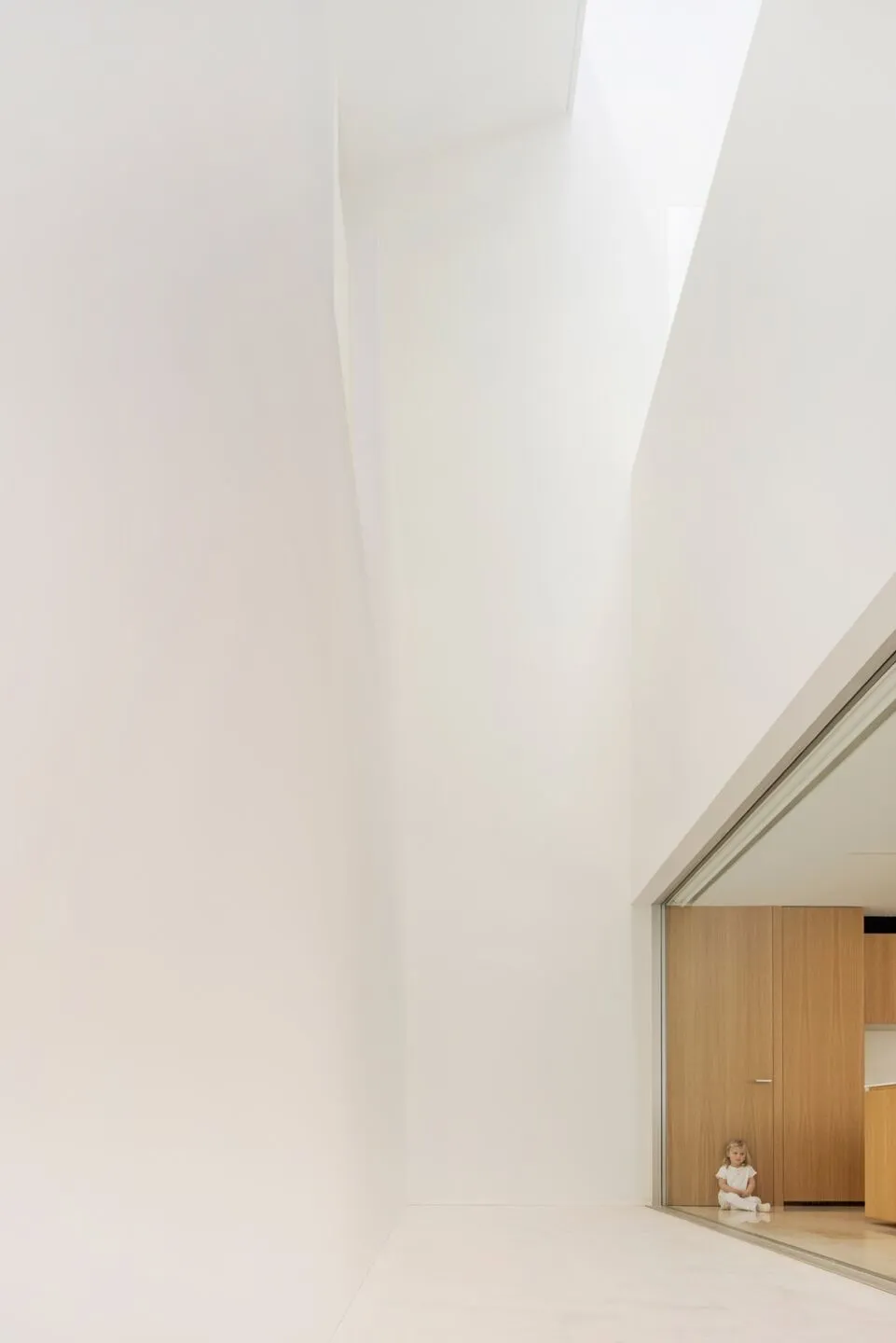 A minimalist living room with white concrete walls and a high ceiling.