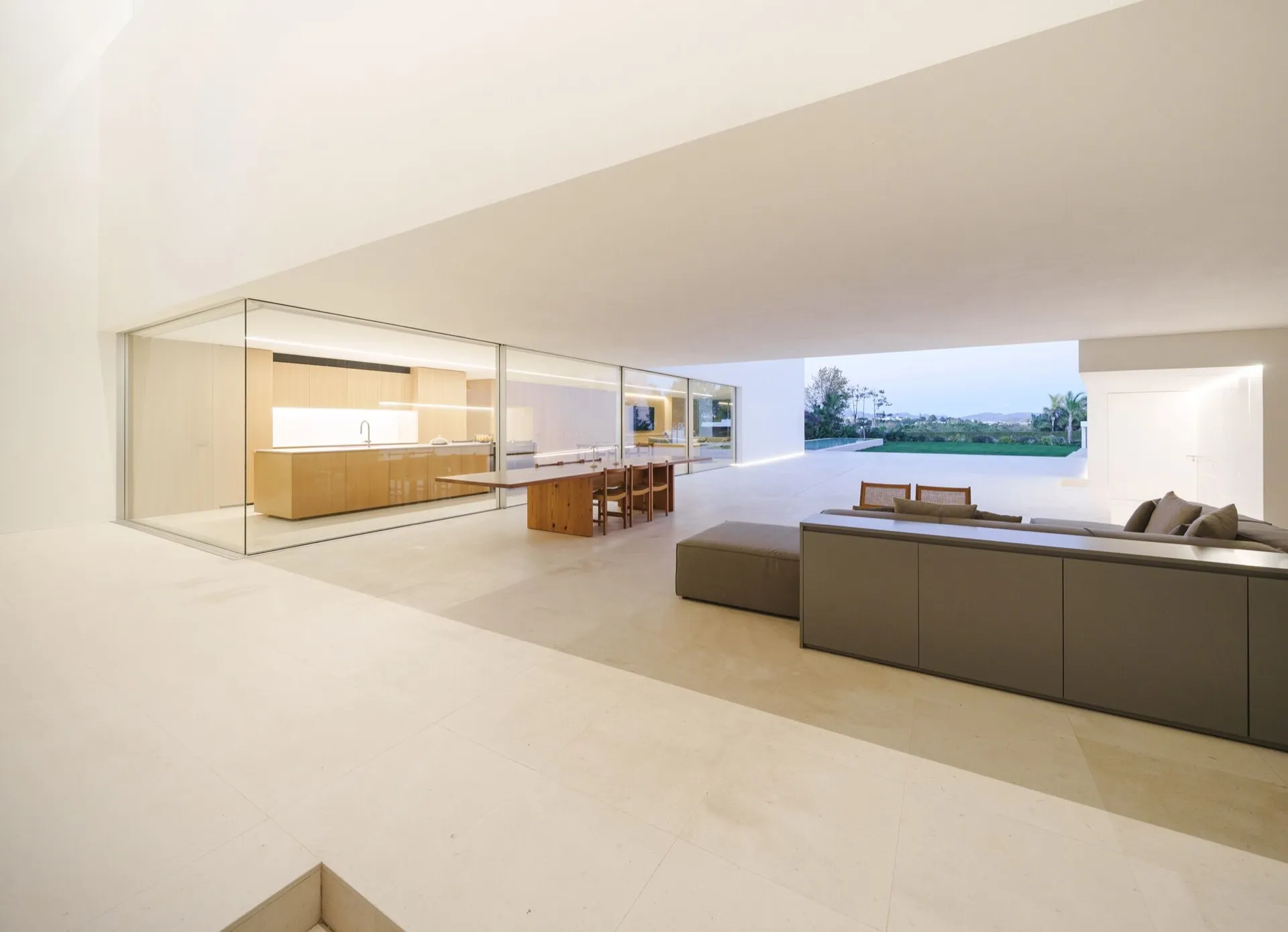 Modern minimalist living room with white walls and floor-to-ceiling windows overlooking an outdoor area.