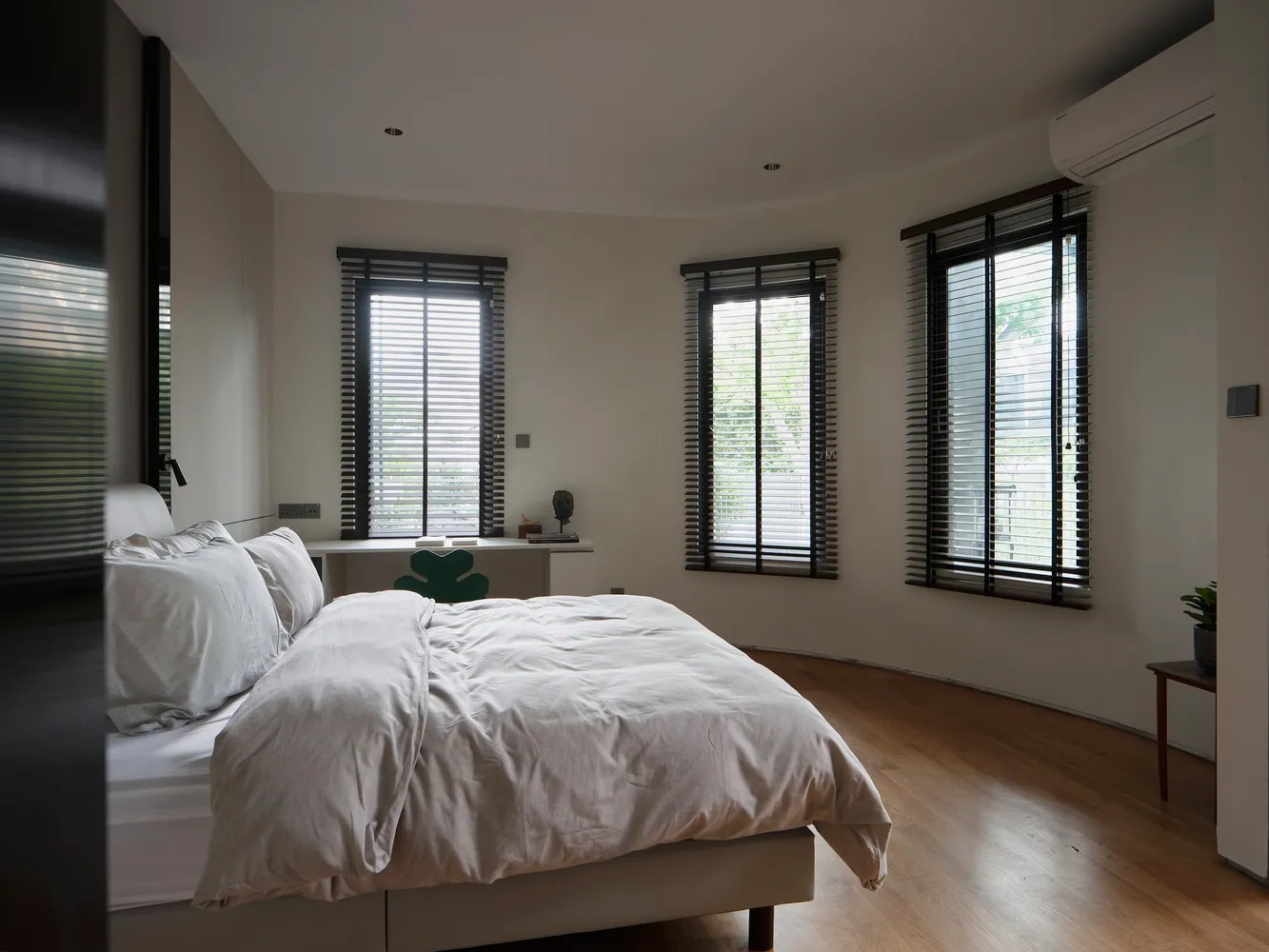 Minimalist bedroom featuring a bed with neutral-toned bedding, wooden flooring, and metal headboard.
