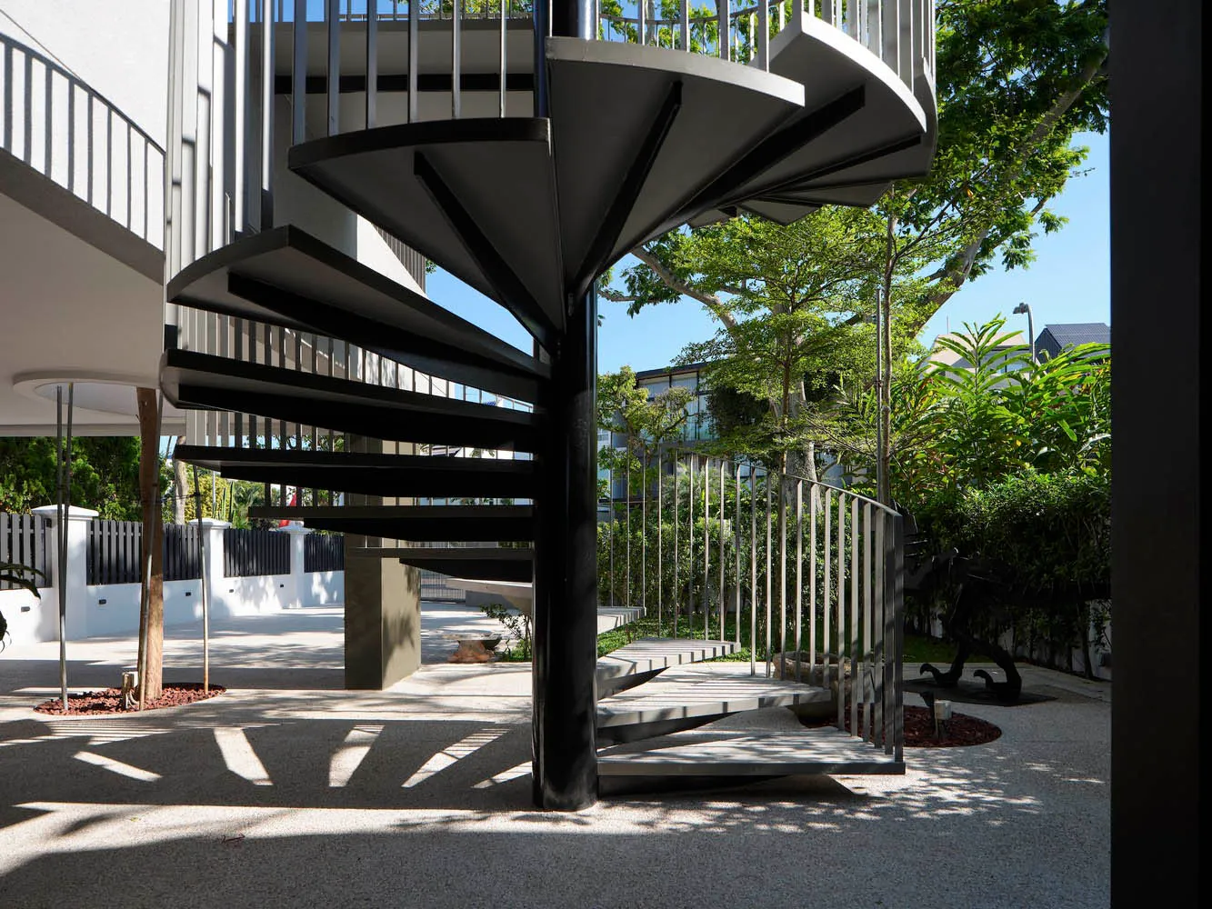 Outdoor spiral staircase with black metal railings and steps, framed by greenery and trees.