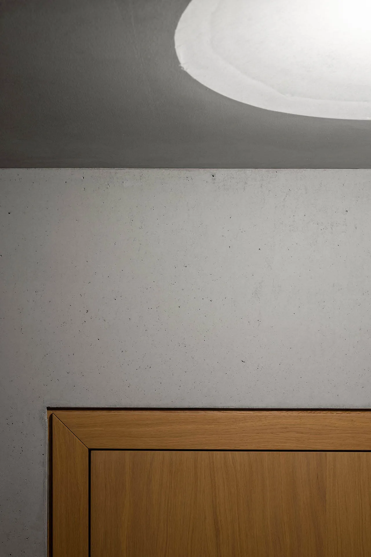 A minimalist bedroom interior featuring concrete walls and a wooden door.