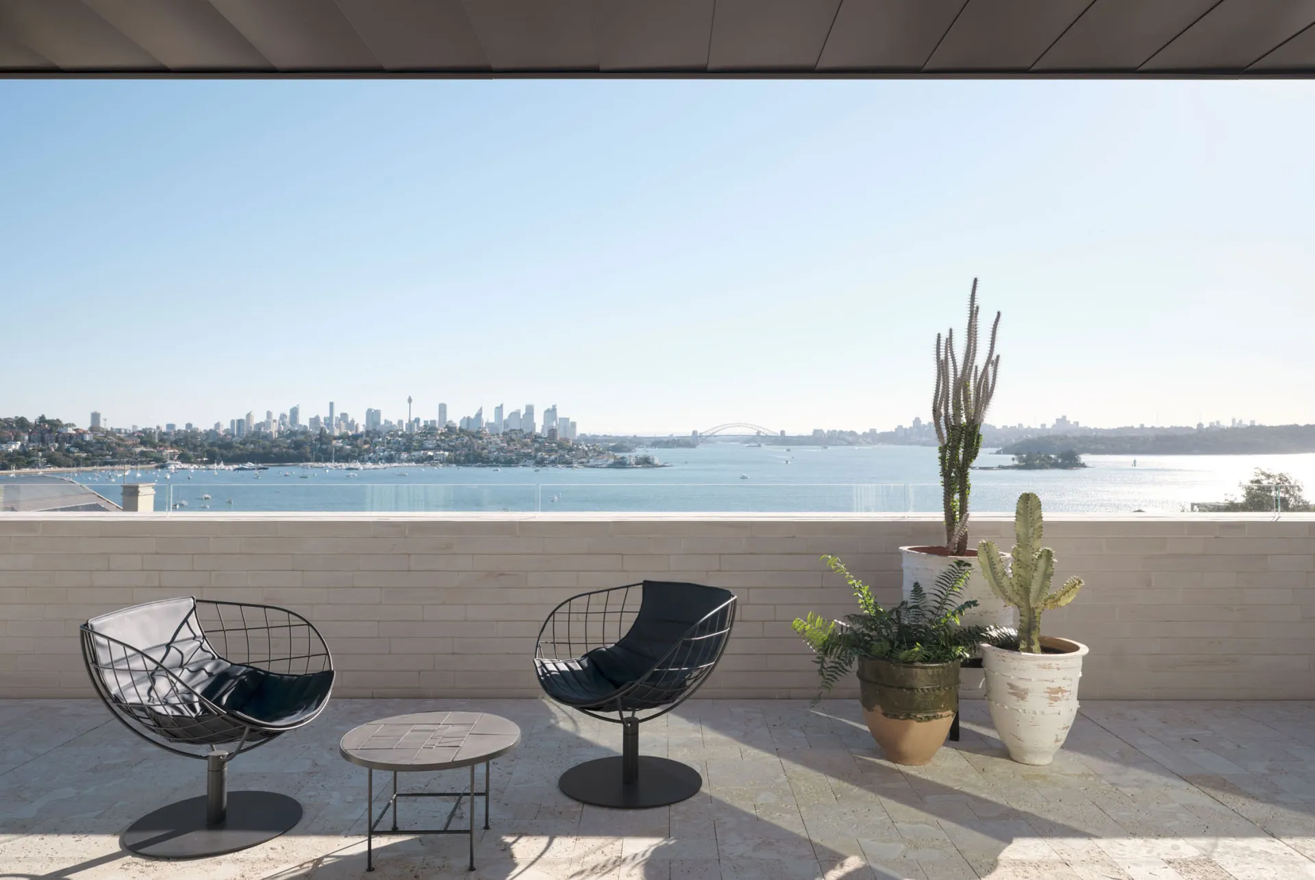 Modern minimalist outdoor lounge area featuring concrete furniture and a panoramic view of a city skyline and waterfront.
