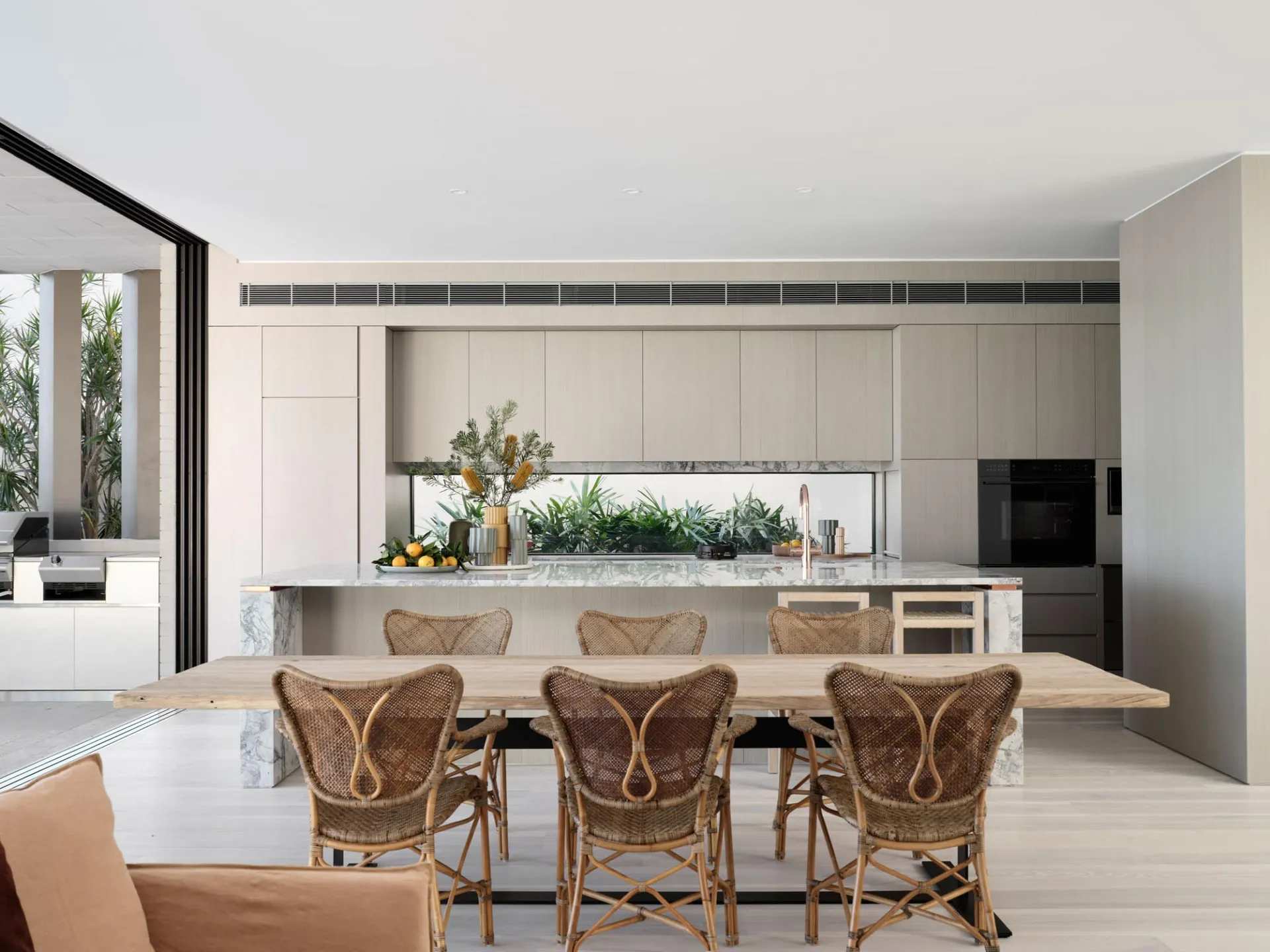Modern residential kitchen featuring marble countertops and dining table with rattan chairs.