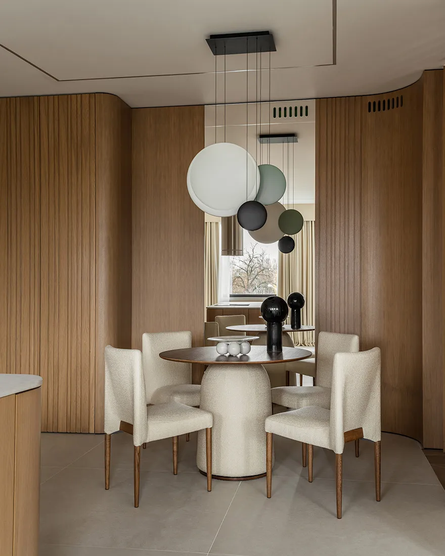 Modern dining room with round wooden table, upholstered chairs, and contemporary lighting fixtures.