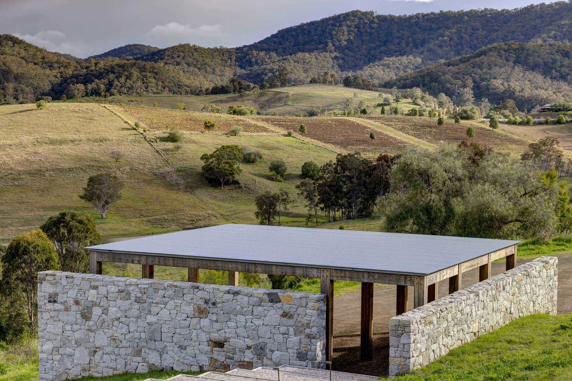A modern industrial-style building exterior with a metal roof and stone walls in a rural setting.